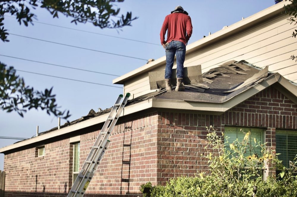 Inspector on the roof of a brick home checking shingles and flashing