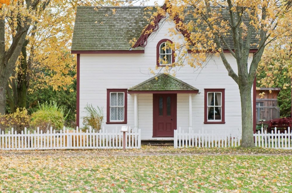 White two-story house with a picket fence under autumn maples